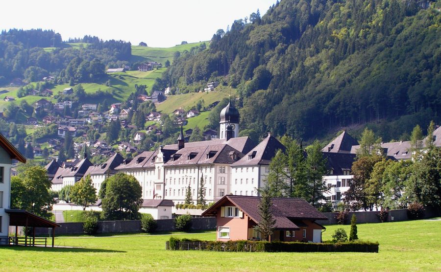 The baroque buildings of Engelberg Monastery below a forested slope